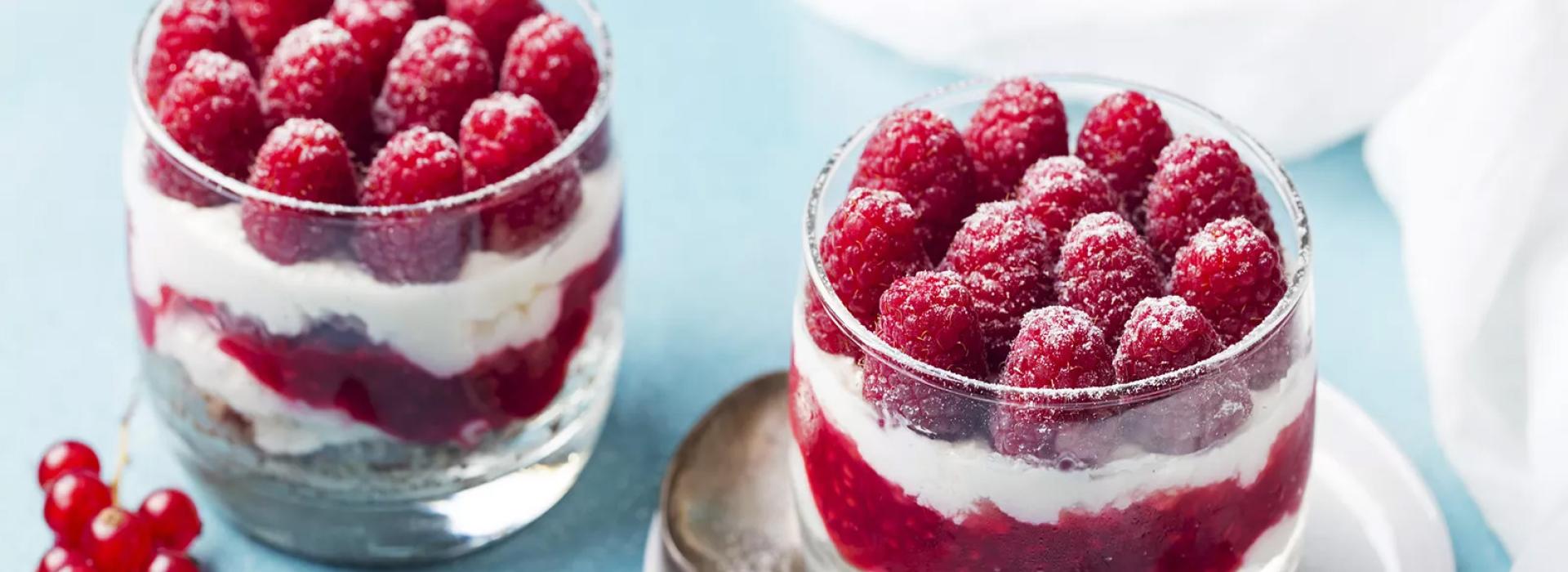 Delizioso dessert con lamponi freschi, panna e frutti di bosco in bicchiere.