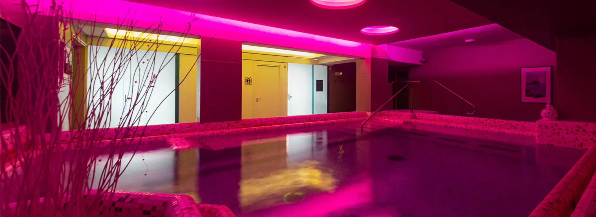 Piscina interna con illuminazione rosa e design moderno.