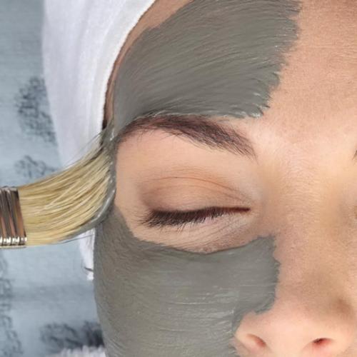 Maschera viso applicata con pennello su pelle, persona rilassata con asciugamano bianco.