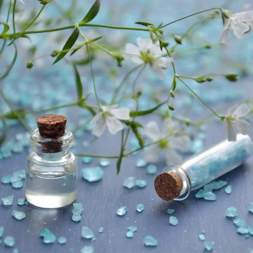 Fiori bianchi, cristalli blu e boccette di vetro su sfondo grigio.