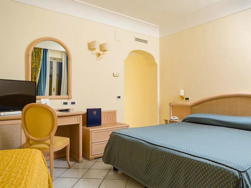 Camera d'albergo con letto matrimoniale, scrivania, sedia e TV, arredamento classico.