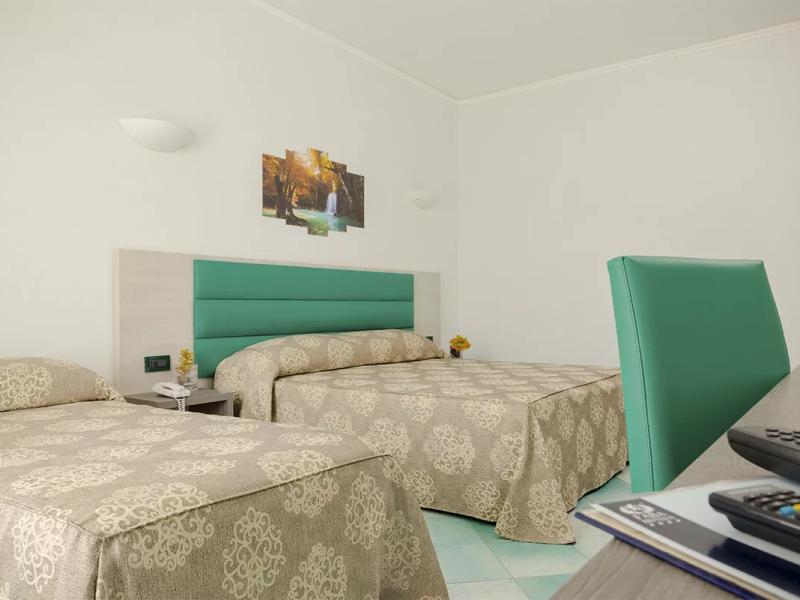Camera d'albergo con due letti, decorazioni beige e sedia verde.