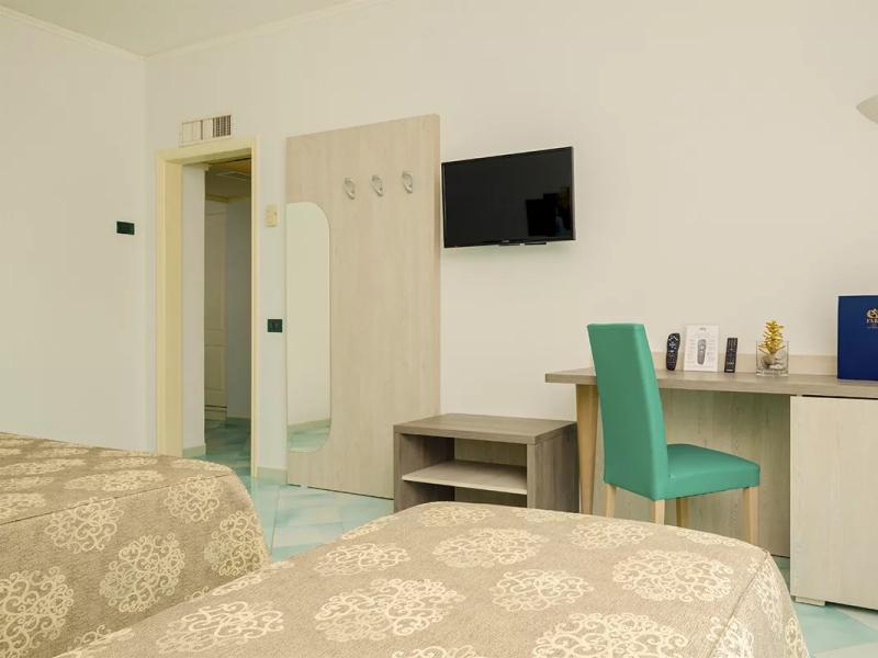 Camera d'albergo con TV, scrivania, sedia verde e letto decorato.