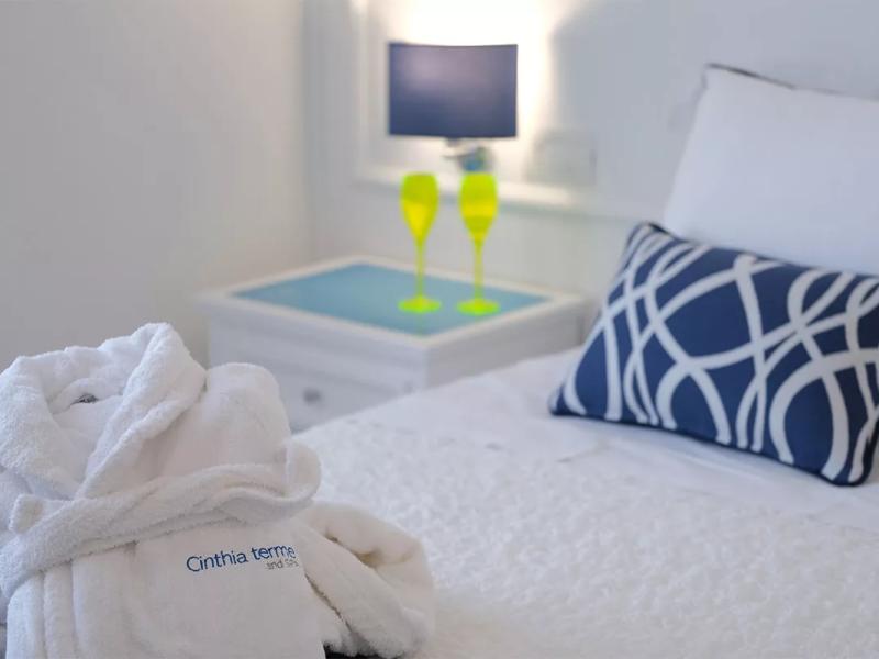 Accogliente camera da letto con accappatoio, cuscino decorativo e bicchieri colorati.