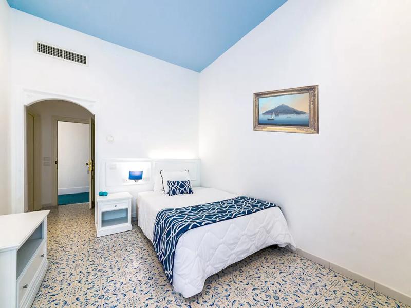 Camera luminosa con letto singolo, decorazioni blu e pavimento piastrellato.