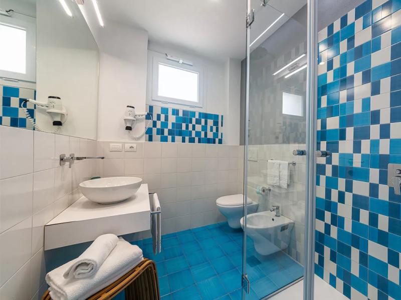 Bagno moderno con piastrelle blu, lavabo angolare e doccia in vetro.