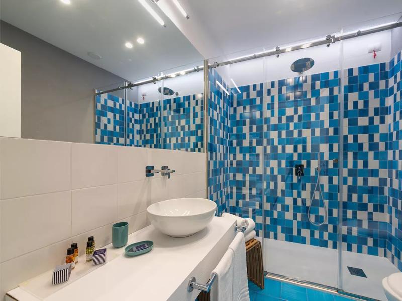 Bagno moderno con piastrelle blu, lavabo bianco e doccia a vetro.
