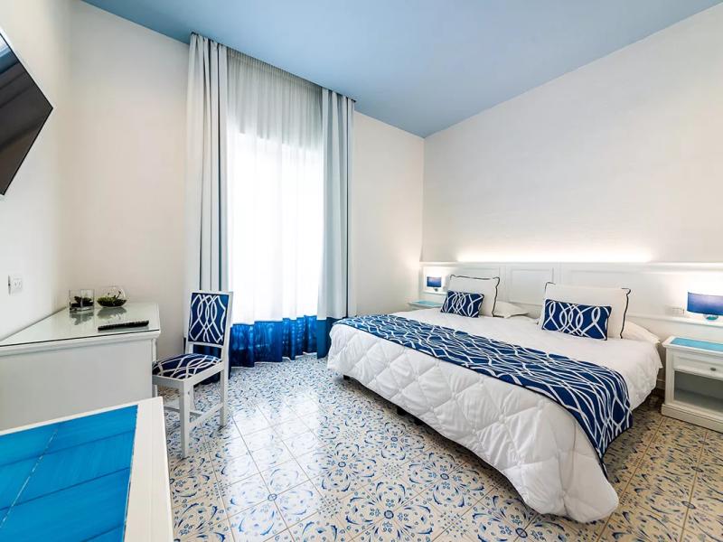 Camera luminosa con decorazioni blu e bianche, letto matrimoniale e TV a parete.