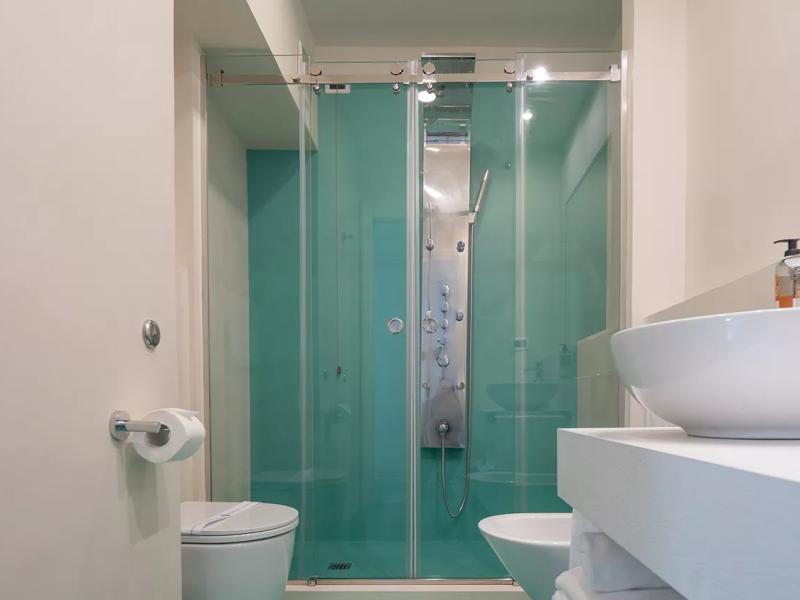 Bagno moderno con doccia in vetro, lavabo bianco e pareti verde acqua.