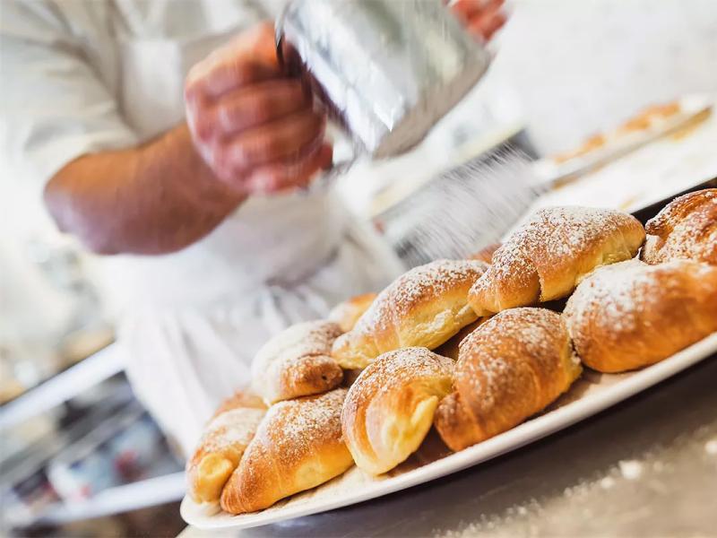 Un pasticcere spolvera zucchero a velo su cornetti appena sfornati.