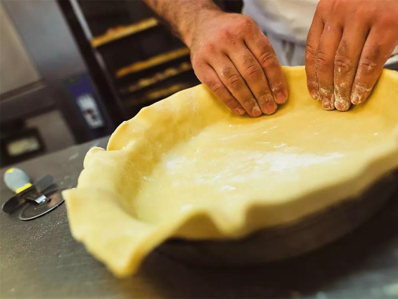 Persona prepara una crostata, stendendo la pasta in una teglia rotonda.