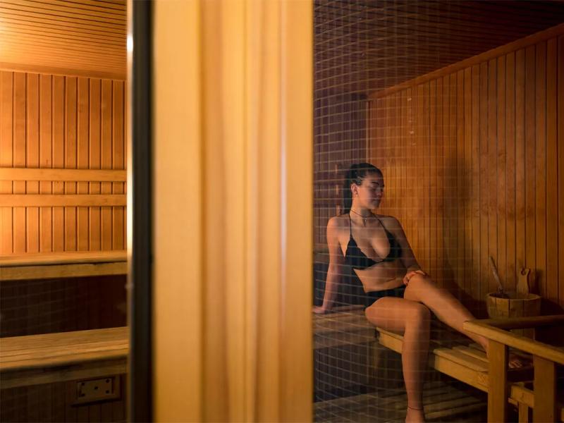 Donna rilassata in sauna di legno, indossa un bikini nero.