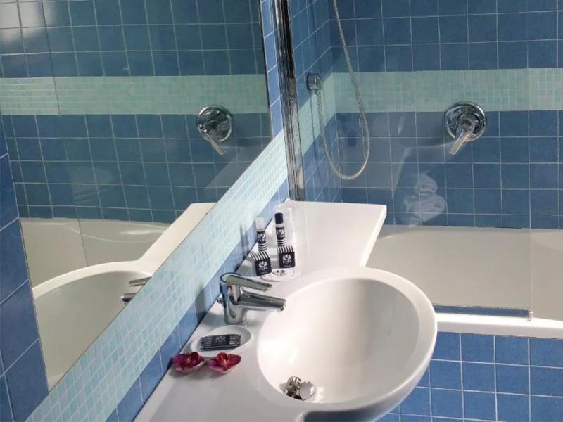 Bagno moderno con piastrelle blu, lavabo bianco e accessori eleganti.